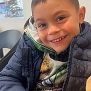 Zack a rejoint le concours — aidez-le/la à gagner de superbes lots ! child, boy, smile, jacket, hoodie, indoors, window, christmas_tree, festive, happy, portrait, face, clothing, casual, young, warm, cozy, seated, cute, holiday