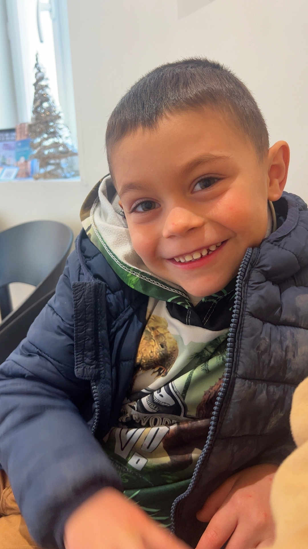 Zack a rejoint le concours — aidez-le/la à gagner de superbes lots ! child, boy, smile, jacket, hoodie, indoors, window, christmas_tree, festive, happy, portrait, face, clothing, casual, young, warm, cozy, seated, cute, holiday