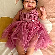 Olivia is registered to the contest to win money with this photo: baby, child, smiling, dress, pink, headband, flower, curly_hair, lying_down, happy, cute, infant, tulle, fabric, barefoot, skin, indoors, portrait, person, bedspread