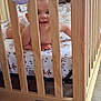 baby, crib, wooden_bars, smile, infant, nursery, bedding, toy, child, crawling, floor, carpet, indoor, cute, person, happy, face, arms, playful, home