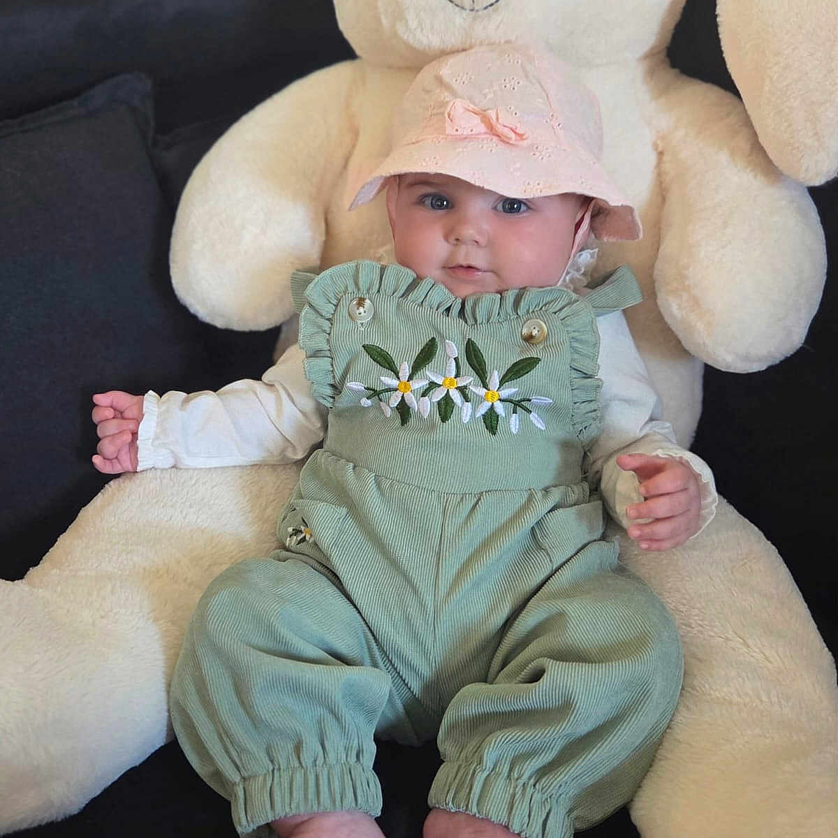 Rose a rejoint le concours — aidez-le/la à gagner de superbes lots ! baby, child, plush_toy, stuffed_animal, bunny, hat, green_overalls, floral_embroidery, cute, infant, sitting, indoor, soft_toy, pink_hat, barefoot, portrait, smiling, small_hands, cozy, couch