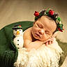 newborn, baby, sleeping, blanket, green, flower_crown, snowman, felt_toy, soft_texture, cozy, portrait, infant, cute, holiday, christmas, decorative, peaceful, indoors, warm_lighting, resting