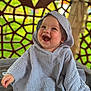 baby, child, hooded_blanket, smiling, happy, portrait, indoor, face, infant, cozy, textured_clothing, cute, sitting, expression, joyful, playful, background_pattern, colorful, soft_light, young