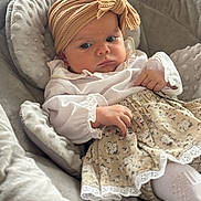 Nevaeh joined the competition — help win amazing prizes! baby, infant, headband, skirt, white_blouse, cushion, plush, soft_fabric, child, portrait, indoors, cute, serious_expression, sitting, hand, face, clothing, patterned_skirt, comfort, headwear