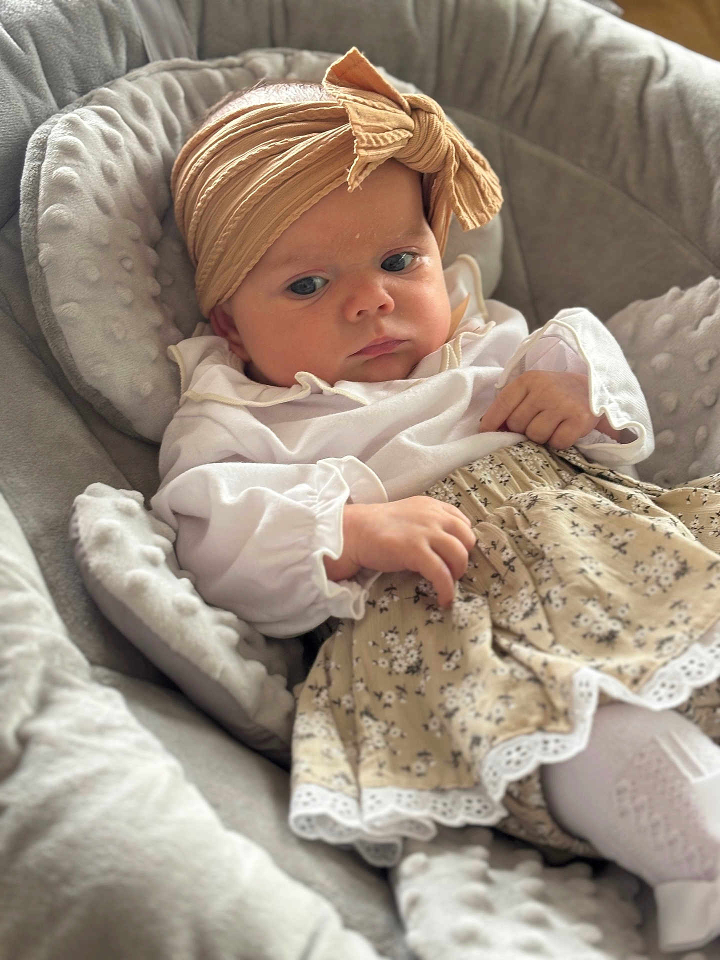 Nevaeh joined the competition — help win amazing prizes! baby, infant, headband, skirt, white_blouse, cushion, plush, soft_fabric, child, portrait, indoors, cute, serious_expression, sitting, hand, face, clothing, patterned_skirt, comfort, headwear