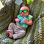 Klay is registered to the contest to win money with this photo: baby, infant, sunglasses, knitted_blanket, green_blanket, baby_bouncer, plush_toy, tie_dye, onesie, pants, barefeet, portrait, indoor, cozy, tiny_hands, newborn, reflection, cute, relaxing, seat