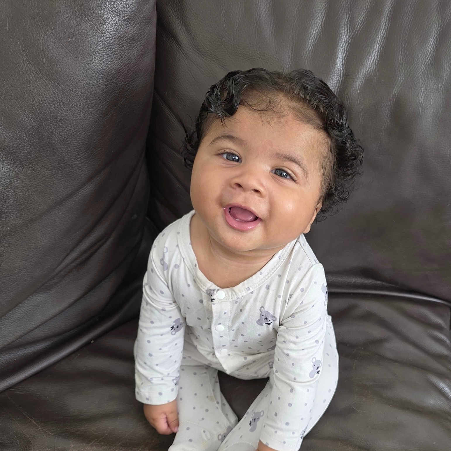 Lkarri is registered to the contest to win money with this photo: baby, child, comfortable, cozy, curly_hair, cute, face, feet, hands, happy, indoor, infant, koala_pattern, leather_couch, onesie, portrait, sitting, smiling, white_clothing, young_child