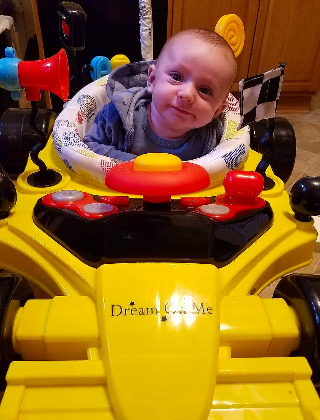 Logan is registered to the contest to win money with this photo: auto_part, automotive_design, baby, baby_toddler_clothing, chair, child, engineering, fun, person, plastic, play, riding_toy, sitting, smile, toddler, vehicle, yellow