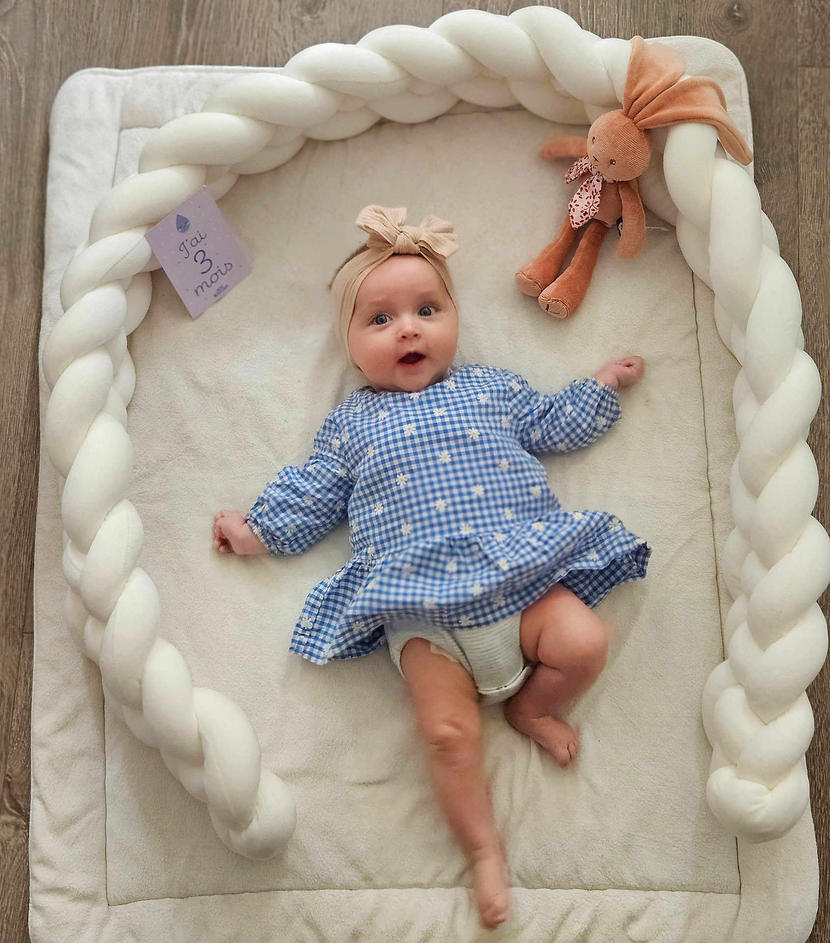 Lou participe au concours pour gagner de l'argent avec cette photo : baby, baby_girl, blue_dress, braided_cushion, child, clothing, cute, face, floor, headband, indoors, infant, lying_down, milestone_card, person, plush_toy, smiling, soft_mat, toy, wood_floor