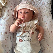 Leya participe au concours pour gagner de l'argent avec cette photo : baby, infant, hat, shirt, cartoon, text, cushion, patterned, blue_pants, hand, face, cute, lying_down, child, indoors, clothing, fabric, expression, young, person