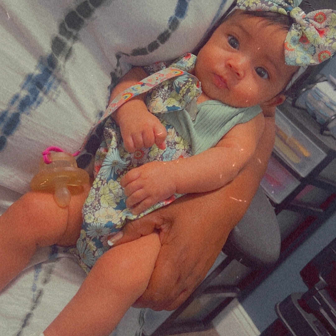 Janeishka joined the competition — help win amazing prizes! adult, arms, baby, bow, child, clothing, floral_pattern, hand, indoor, pacifier, person, portrait, seated, sitting, skin, table, toy, white_sock, woman, young_child