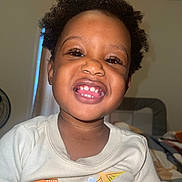 Ezrah is registered to the contest to win money with this photo: bedroom, casual, child, clothing, curly_hair, cute, dinosaur_print, face, fan, happy, indoor, light, person, portrait, room, shirt, smile, teeth, toddler, young_child