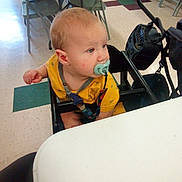 Jordan joined the competition — help win amazing prizes! baby, pacifier, high_chair, yellow_shirt, indoor, table, chair, floor, child, infant, person, seated, looking_away, daylight, curious, plastic, feeding, toddler, casual, room