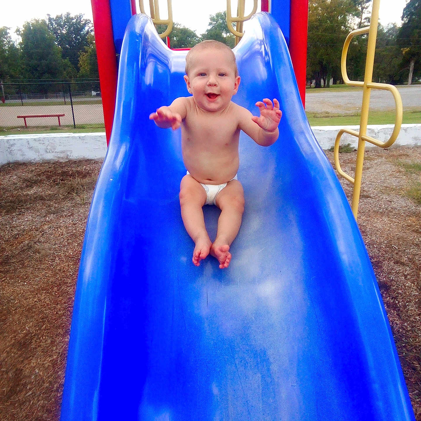 Jordan joined the competition — help win amazing prizes! baby, bare_chest, blue_slide, child, climbing_frame, daylight, diaper, fun, grass, happy, infant, joy, outdoor, park, play_equipment, playground, recreation, slide, smiling, trees