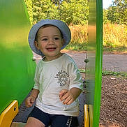 Gabin participe au concours pour gagner de l'argent avec cette photo : child, toddler, smiling, slide, playground, hat, shorts, outdoor, green, sunlight, trees, nature, summer, happy, park, playing, clothing, fun, person, recreation