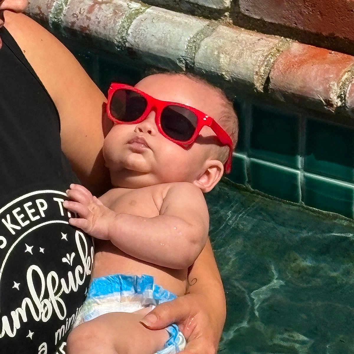 Phoenix joined the competition — help win amazing prizes! baby, infant, child, sunglasses, red_sunglasses, diaper, being_held, adult, portrait, poolside, water, tiles, brick_wall, outdoor, sunlight, close_up, relaxed, funny, fashion, family