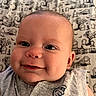 Phoenix is registered to the contest to win money with this photo: baby, infant, child, smiling, portrait, close_up, face, eyes, lying_down, gray_clothing, blanket, fabric, patterned_background, cemetery_pattern, cozy, indoor, happy, photography, head, baby_clothing