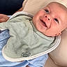 baby, smiling, blue_eyes, bib, blue_clothing, cushion, indoor, infant, person, happy, portrait, closeup, child, cute, skin, head, face, seat, resting, comfort
