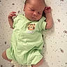 newborn, baby, sleeping, onesie, green_clothing, tiger_patch, dandelion_pattern, crib, soft_lighting, peaceful, infant, cute, cozy, resting, small_hands, white_socks, fabric, bed, portrait, indoor