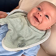 Noah is registered to the contest to win money with this photo: baby, smiling, indoor, bib, blue_clothing, cushion, infant, happy, face, person, portrait, closeup, light_blue, furniture, door, hand, skin, head, baby_bib, baby_clothes