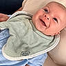 baby, smiling, indoor, bib, blue_clothing, cushion, infant, happy, face, person, portrait, closeup, light_blue, furniture, door, hand, skin, head, baby_bib, baby_clothes