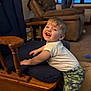 toddler, child, smile, happy, indoor, rocking_chair, wood, cushion, white_shirt, camouflage_pants, living_room, carpet, furniture, person, baby_teeth, window, recliner, curtains, toy, playing