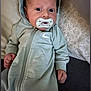 Carter is registered to the contest to win money with this photo: baby, infant, pacifier, hoodie, gray_clothing, lying_down, pillow, floral_pattern, face, wide_eyes, cute, indoors, person, child, young_baby, casual_wear, portrait, expression, cozy, closeup