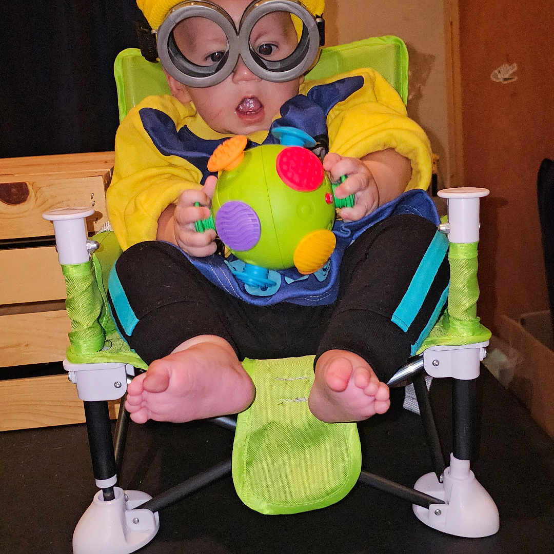Blake is registered to the contest to win money with this photo: accessories, baby, bodypart, cap, clothing, coat, costume, face, furniture, glasses, goggles, hat, head, indoors, interiordesign, person, photography, portrait, table, toy