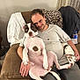 man, dog, large_dog, small_dog, couch, indoor, leopard_print_blanket, casual_clothing, brown_couch, relaxed, pet, domestic, home_interior, seated, hand, floor, curtains, bottle, white_tshirt, friendly