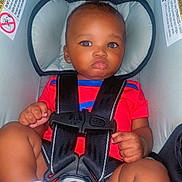Prophet is registered to the contest to win money with this photo: baby, car_seat, child, infant, safety_harness, red_clothing, socks, seat_belt, cute, indoors, young_child, face, portrait, straps, head_support, hands, legs, expression, seat, person