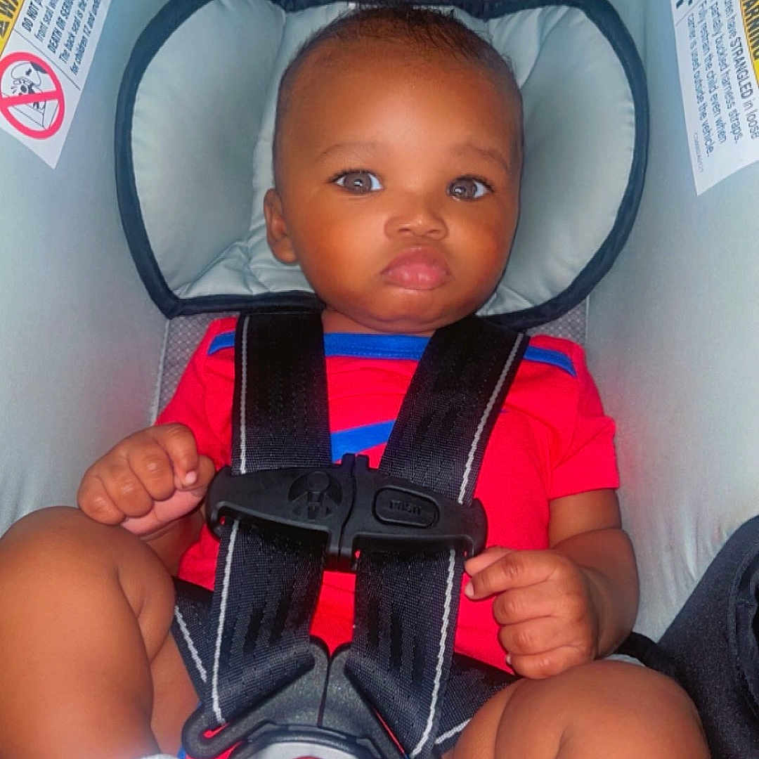 Prophet is registered to the contest to win money with this photo: baby, car_seat, child, cute, expression, face, hands, head_support, indoors, infant, legs, person, portrait, red_clothing, safety_harness, seat, seat_belt, socks, straps, young_child