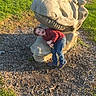 casual_clothing, child, daytime, dinosaur_sculpture, excited, fun, grass, happy, jeans, nature, outdoor, park, playing, red_shirt, sculpture, sidewalk, smiling, sunlight, woodchips, young_boy