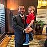 beard, carpet, casual, child, formal, glass, happy, holding, indoor, jeans, lamp, man, people, plant, portrait, red_shirt, smile, suit, window, wood_floor