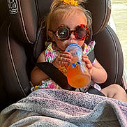 Vivian is registered to the contest to win money with this photo: toddler, child, sunglasses, car_seat, bottle, drink, blanket, yellow_bow, graco, seatbelt, sunlight, window, floral_dress, baby, cute, indoors, seat, hair, person, baby_drink