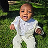 Jeremiah is registered to the contest to win money with this photo: baby, child, grass, outdoor, sunlight, white_suit, tuxedo, smiling, happy, portrait, cute, person, nature, greenery, baby_clothing, one_person, sitting, daylight, formal_wear, young_child