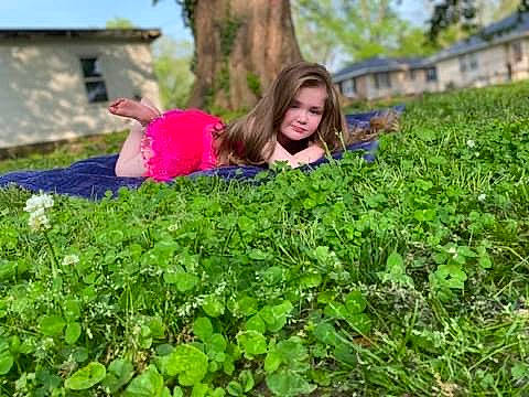 Annabelle is registered to the contest to win money with this photo: agriculture, eyewear, field, garden, grass, grassland, groundcover, happy, landscape, leaf, leisure, magenta, people_in_nature, person, plant, plantation, shrub, sitting, soil, tree