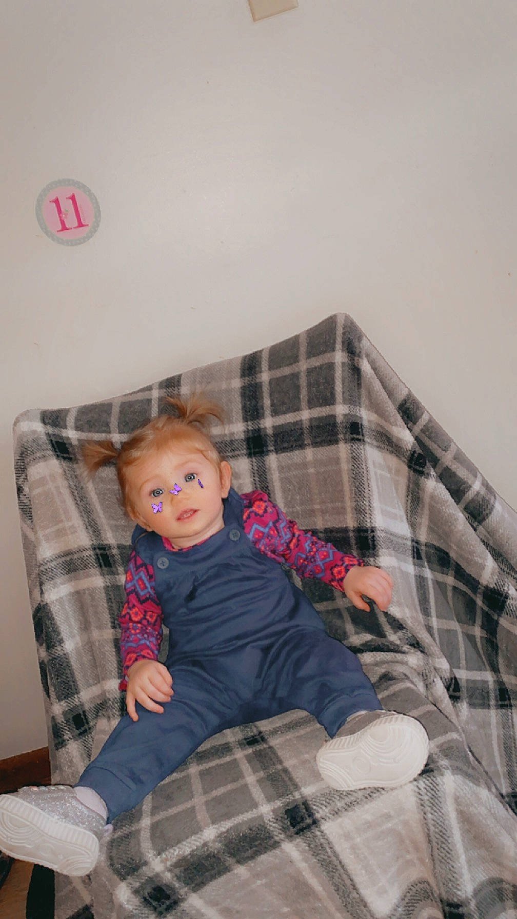Aspen is registered to the contest to win money with this photo: bed, child, comfort, couch, design, flooring, fun, lap, linens, living_room, pattern, person, plaid, sitting, sleeve, smile, sock, tartan, textile, toddler