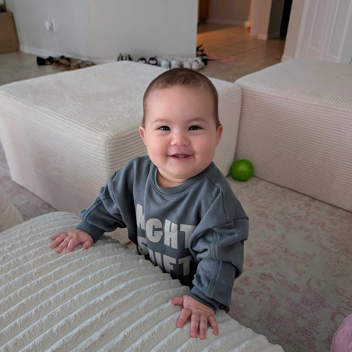 Miyu is registered to the contest to win money with this photo: baby, blanket, child, couch, furniture, gray_shirt, green_ball, hallway, happy, home, indoors, infant, living_room, ottoman, photography, portrait, shoes, sitting, smiling, standing