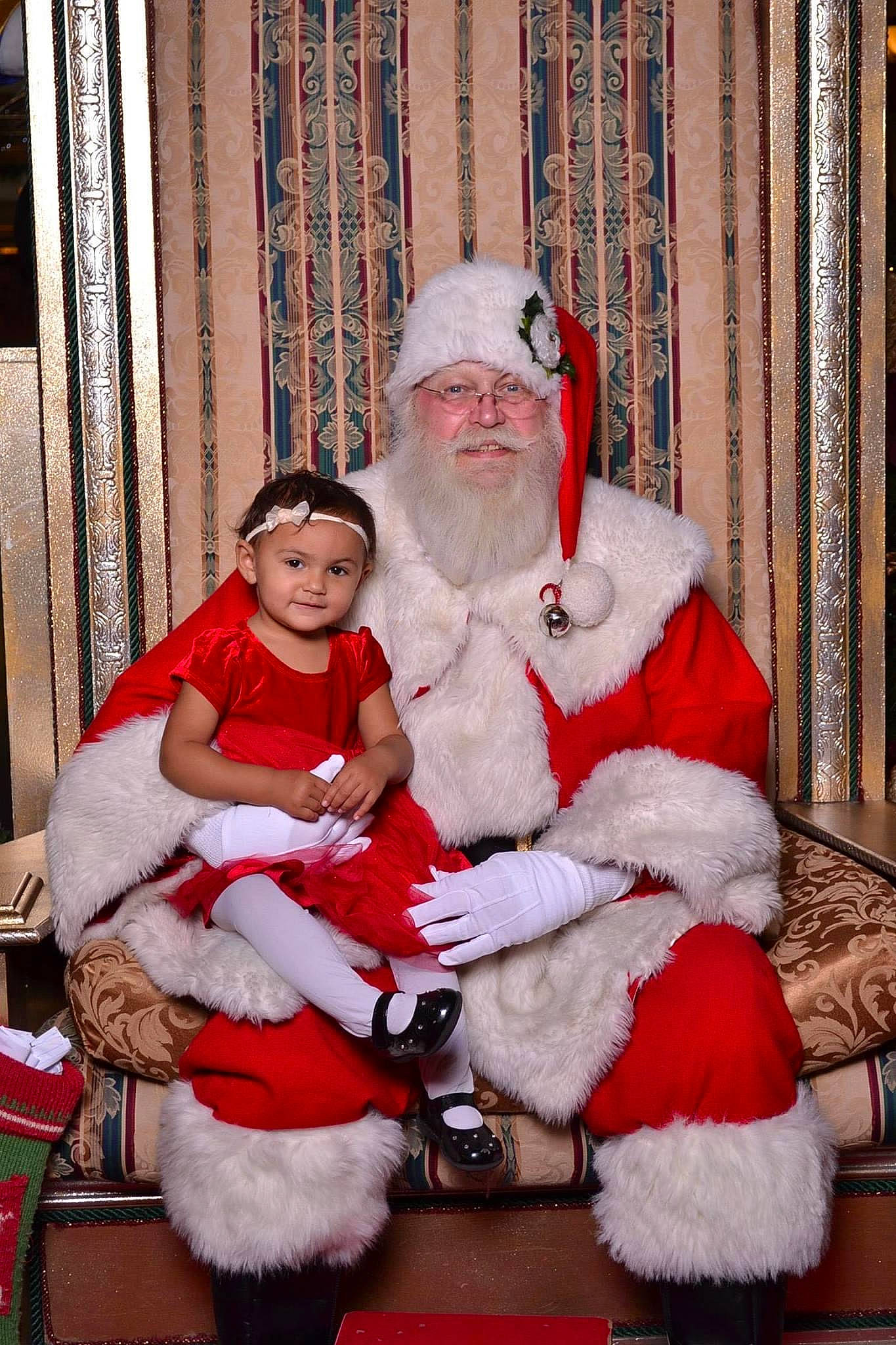 Arianna is registered to the contest to win money with this photo: baby, beard, christmas, costume_hat, curtain, event, facial_expression, fictional_character, fun, fur, fur_clothing, happy, hat, headwear, holiday, lap, person, red, santa_claus, toddler