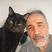 Nabih participe au concours pour gagner de l'argent avec cette photo : animal, beard, black_cat, casual_clothing, closeup, companion, domestic_animal, expression, face, feline, friendship, gray_hair, human, indoor, looking, man, pet, portrait, whiskers, yellow_eyes