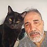 animal, beard, black_cat, casual_clothing, closeup, companion, domestic_animal, expression, face, feline, friendship, gray_hair, human, indoor, looking, man, pet, portrait, whiskers, yellow_eyes