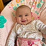 Theia is registered to the contest to win money with this photo: baby, infant, smiling, child, floral_pattern, baby_chair, indoor, cute, portrait, seated, pink, clothing, toy, happy, person, face, young_child, cozy, home, comfort