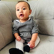 Aitana joined the competition — help win amazing prizes! baby, child, couch, gray, houndstooth, clothing, sitting, indoor, cute, portrait, face, expression, black_shoes, white_tights, furniture, young_child, adorable, curious, small_hands, earrings