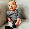 baby, child, couch, gray, houndstooth, clothing, sitting, indoor, cute, portrait, face, expression, black_shoes, white_tights, furniture, young_child, adorable, curious, small_hands, earrings