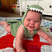 Cole joined the competition — help win amazing prizes! baby, child, smiling, dinosaur_costume, green_clothing, crawling, quilt, colorful, indoor, carpet, toy, furniture, cabinet, wooden, happy, cute, face, cheeks, arm, play