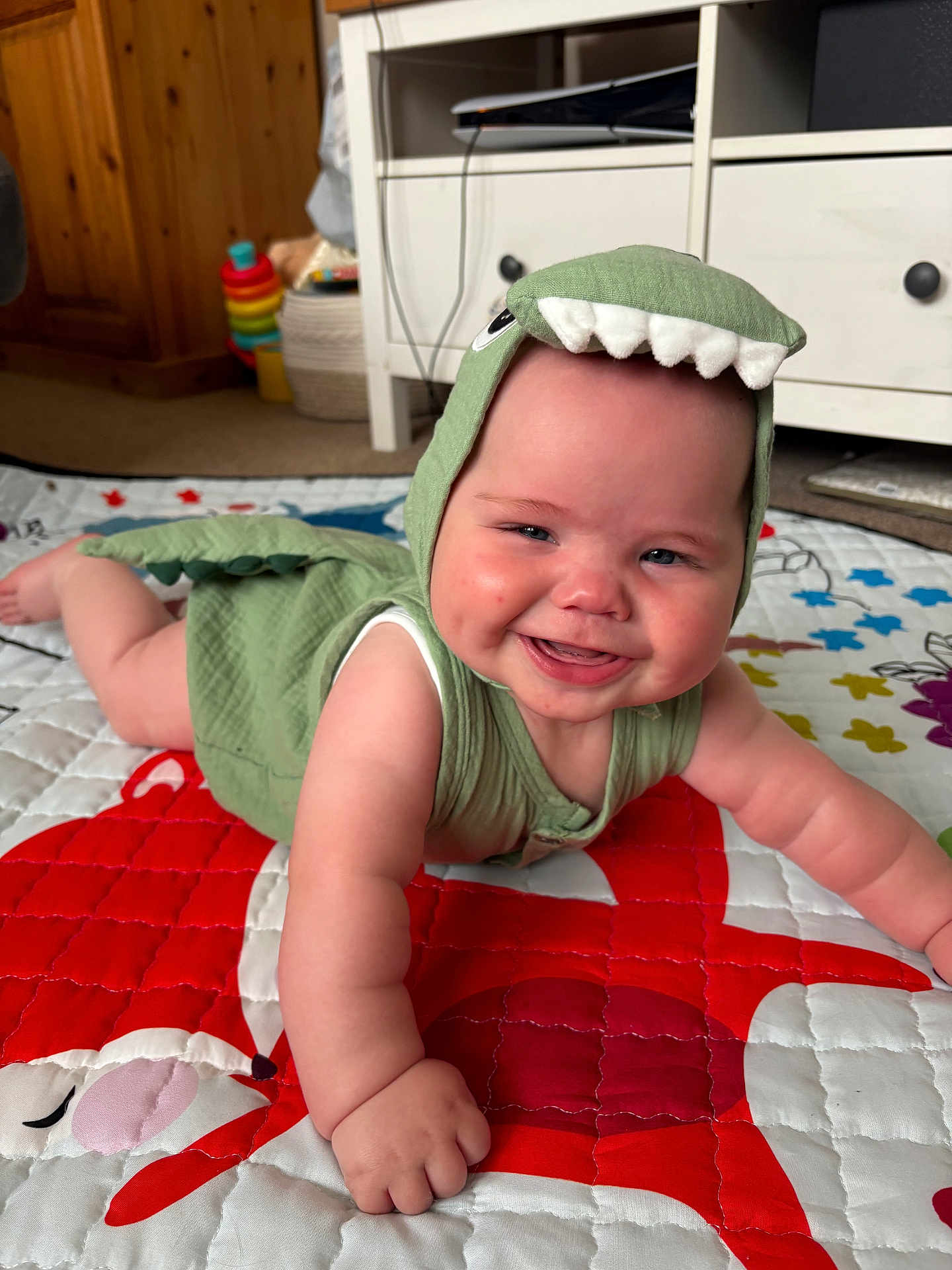 Cole joined the competition — help win amazing prizes! baby, child, smiling, dinosaur_costume, green_clothing, crawling, quilt, colorful, indoor, carpet, toy, furniture, cabinet, wooden, happy, cute, face, cheeks, arm, play