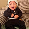 baby, child, infant, smiling, happy, portrait, sitting, indoor, couch, blanket, hat, knit_hat, black_clothing, onesie, pants, buttons, hands, face, home, cozy