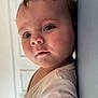 baby, cheeks, child, close_up, curious, cute, expression, eyelashes, face, head, indoor, infant, leaning, person, portrait, skin, soft_light, wall, white_clothing, young