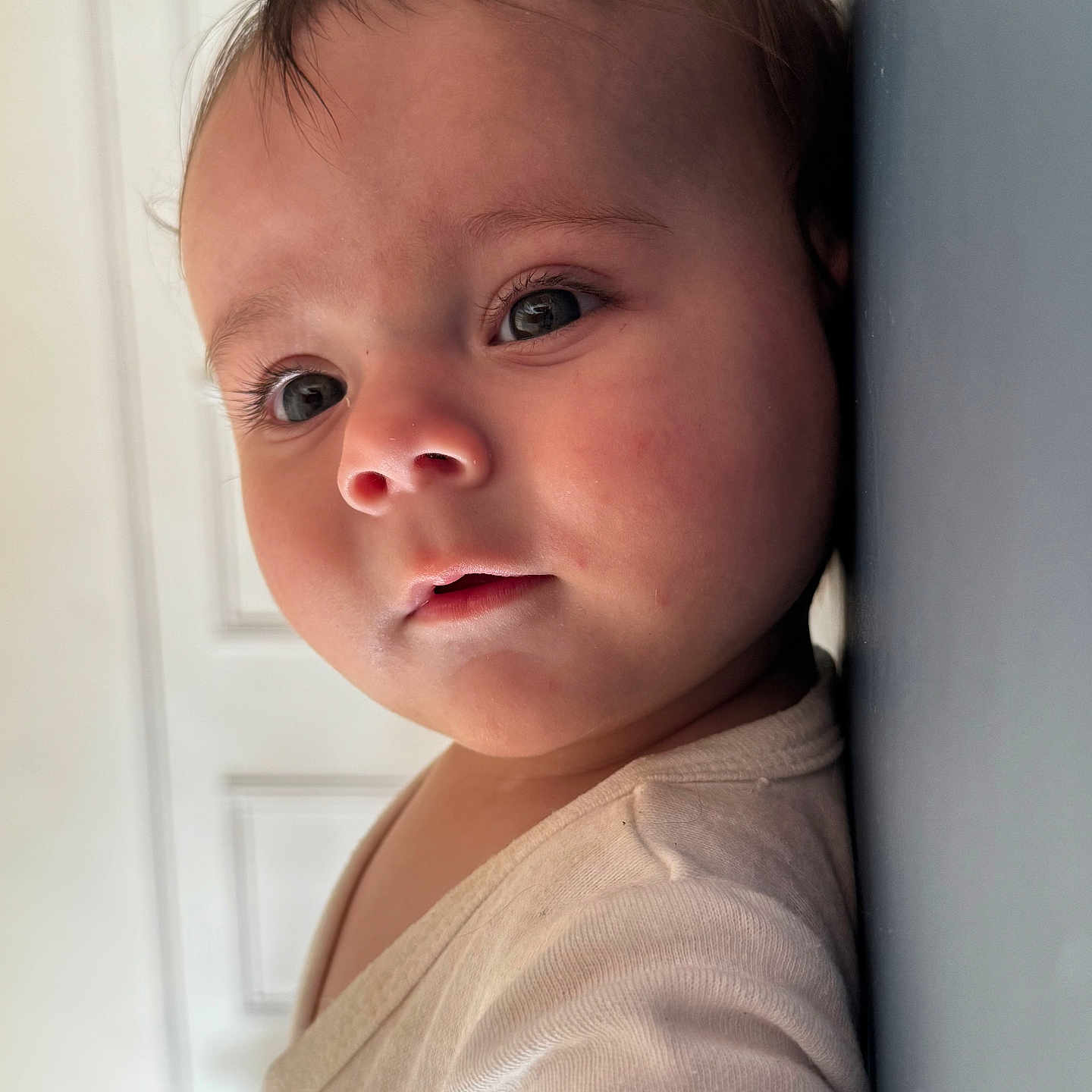 Mahé a rejoint le concours — aidez-le/la à gagner de superbes lots ! baby, cheeks, child, close_up, curious, cute, expression, eyelashes, face, head, indoor, infant, leaning, person, portrait, skin, soft_light, wall, white_clothing, young