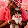 woman, dog, puppy, knitted_hat, pink_shirt, bow_tie, flowers, indoor, portrait, smiling, happy, pet, cute, cozy, home, decor, pink_theme, text_overlay, lighting, holding